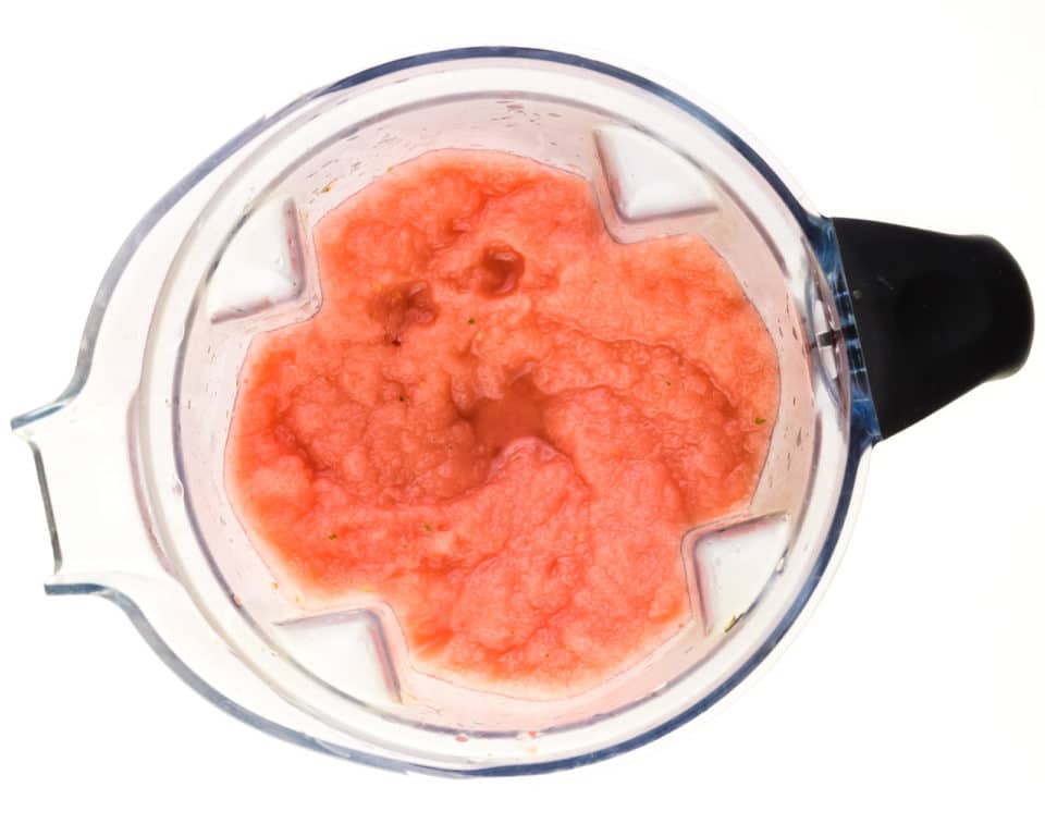A watermelon slushie mixture is in the bottom of a blender jar.