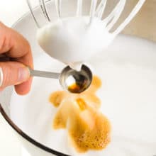 Vanilla is added to whipped cream in a stand mixer.