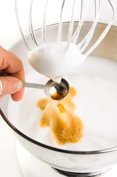 Vanilla is added to whipped cream in a stand mixer.