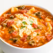 A bowl of tomato-based soup shows noodles and a creamy sauce on top.