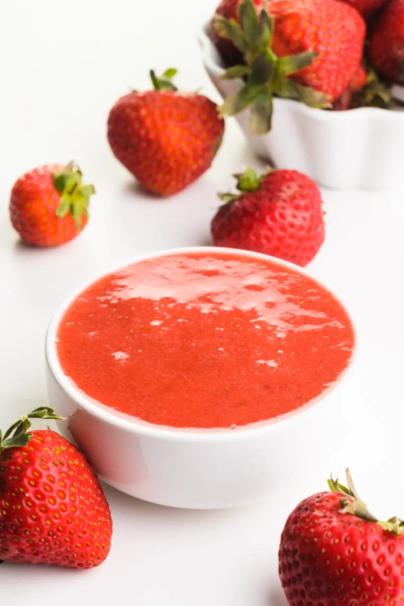A bowl of strawberry sauce has fresh strawberries around it.