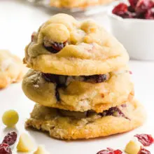 A stack of cookies sits next to ingredients used to make the cookies, like dried fruit and chocolate chips.