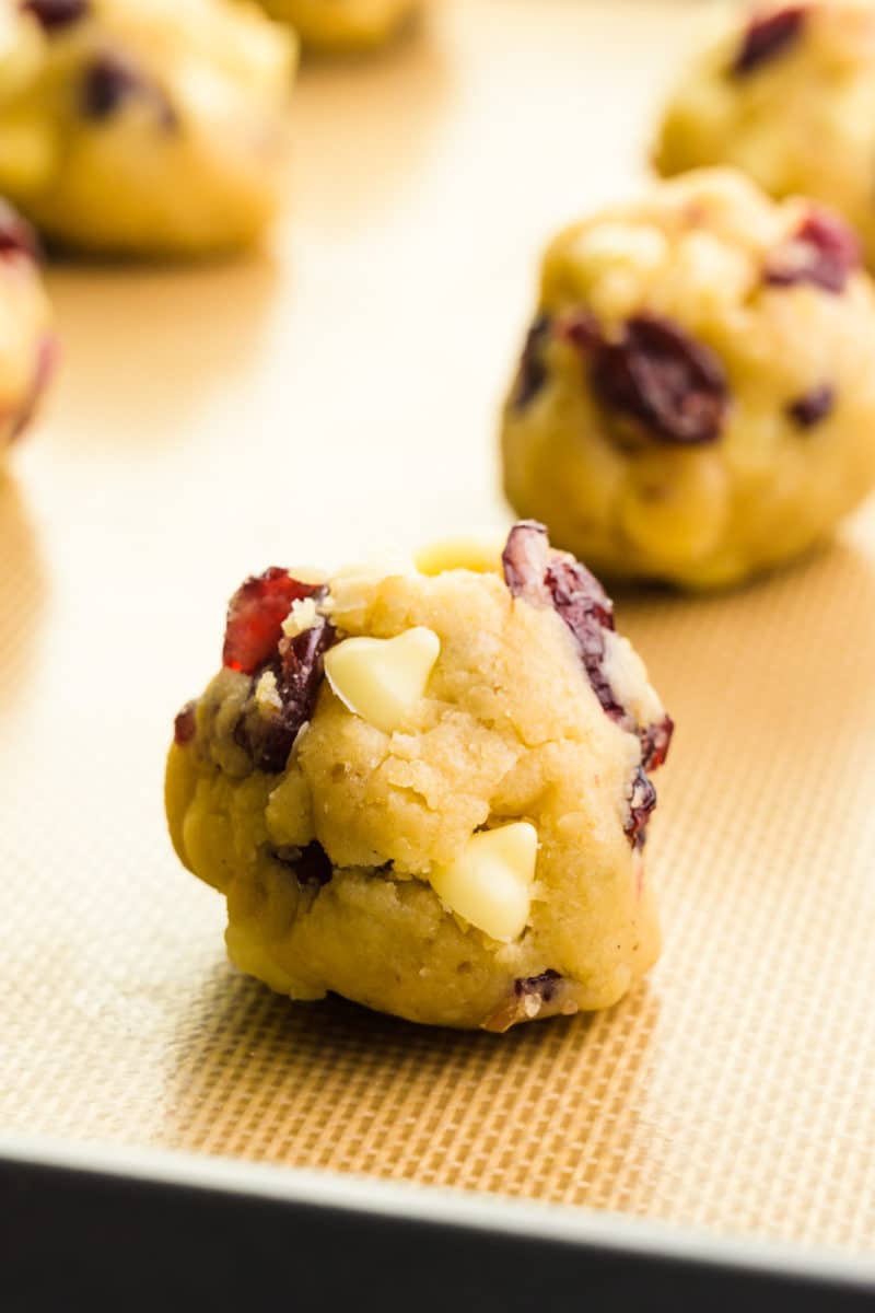 Several unbaked cookie dough balls sit on a baking sheet, ready to go in the oven.