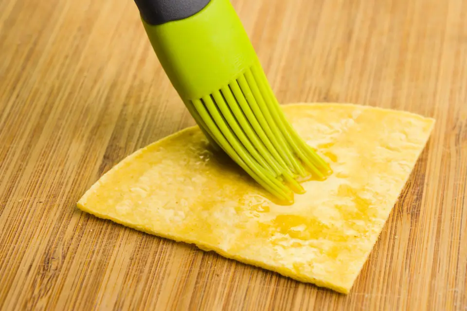Oil is being brushed on a triangular shaped tortilla, preparing it to be fried.
