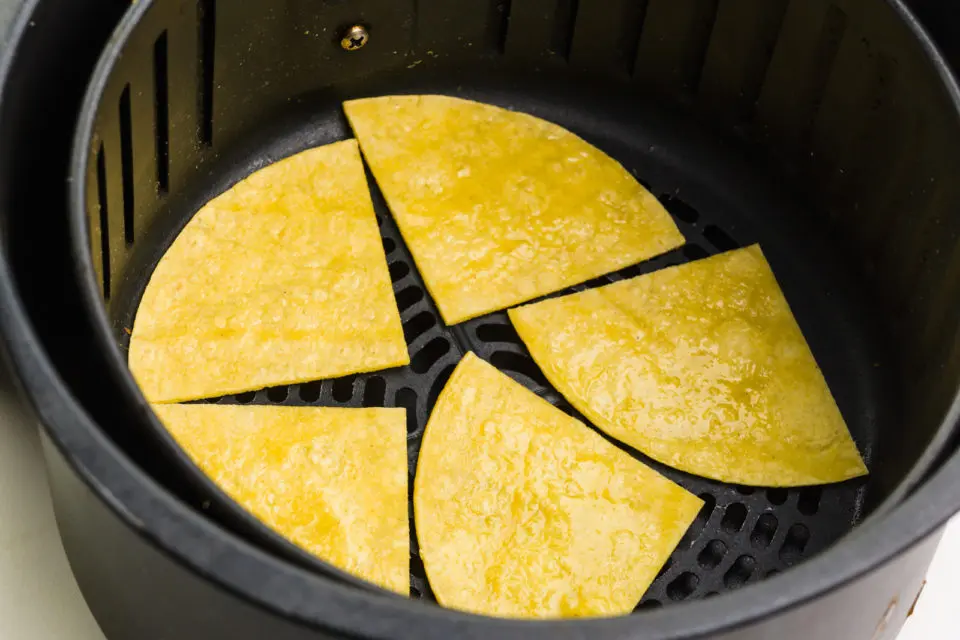 Corn tortilla pieces are in an air fryer basket, getting ready to be fried.