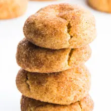 A stack of four snickerdoodles cookies sit one on top of the other, with lots of cinnamon sugar coating. There are several cookies in the background.