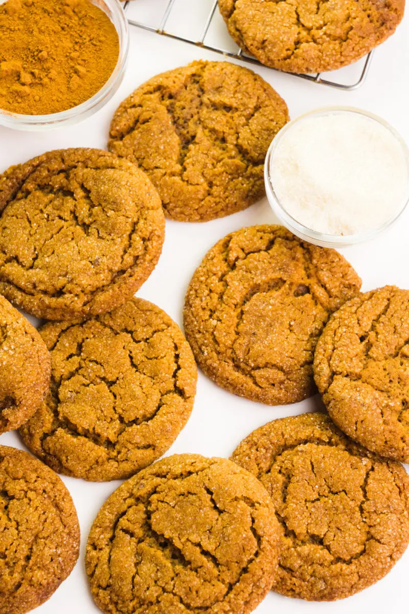 Looking down on several cookies on a white counter. There's a bowl of sugar and cinnamon sitting next to them.
