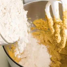 Flour is being poured into a mixing bowl with cookie batter.