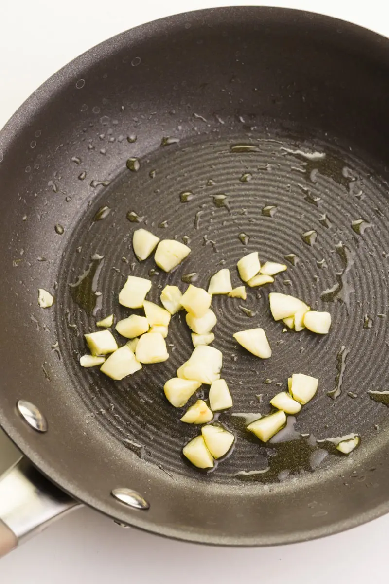 Bits of chopped garlic are being cooked in a skillet with olive oil.