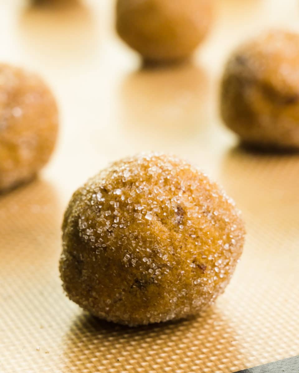 Cookie dough balls have been rolled in sugar and sit on a cookie sheet.