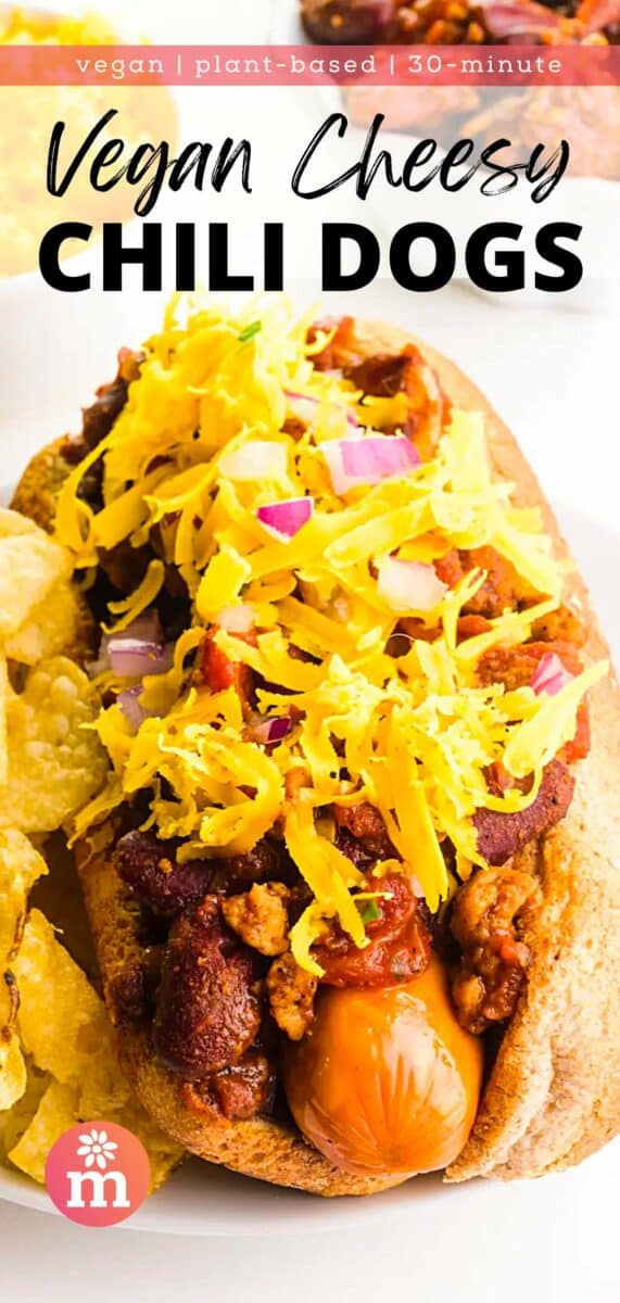 A chili dog in a bun sits on a plate in front of other ingredients. The text reads, vegan, plant-based, 30-minute Vegan Cheesy Chili Dogs.