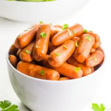 A bowl of roasted carrots has parsley on top and around it. There's a bowl of salad behind it.