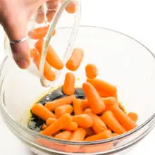 Baby carrots are being tossed into a bowl with a balsamic mixture.