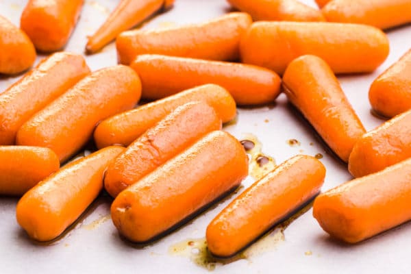 Marinated baby carrots are on a baking sheet.
