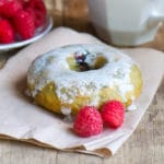 A frosted berry donut sits on a napkin with raspberries next to it
