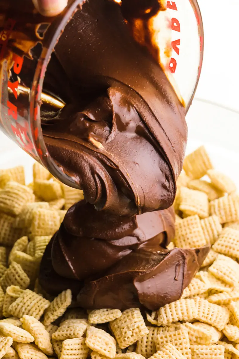 A chocolate mixture is being poured over a bowl full of Chex cereal.