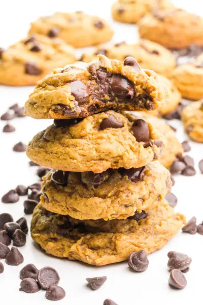 A stack of molasses cookies shows the top one with a bite taken out. There are chocolate chips and more cookies behind the stack.