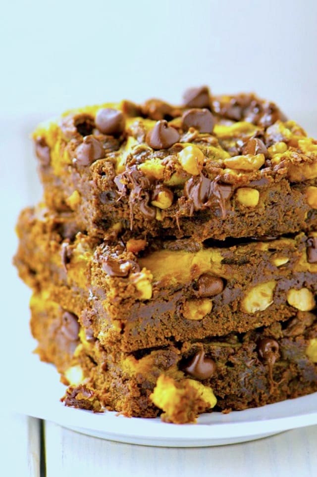 A stack of pumpkin swirl brownies shows melted chocolate chips and chopped nuts throughout.