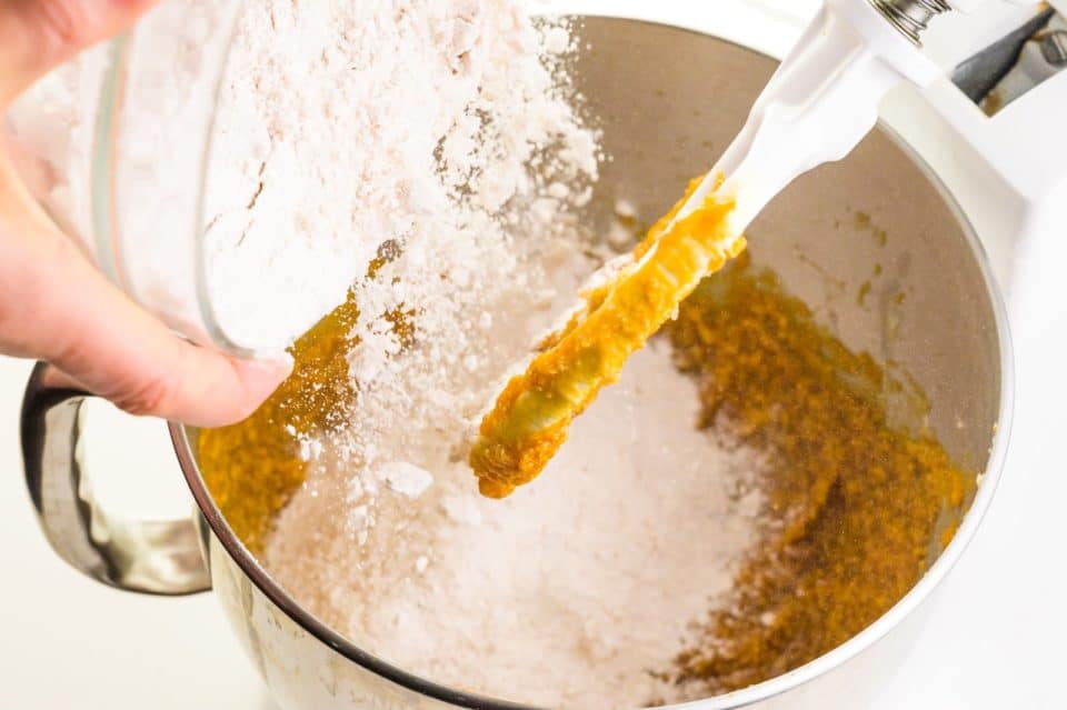 Flour is poured into a mixing bowl with a pumpkin mixture.
