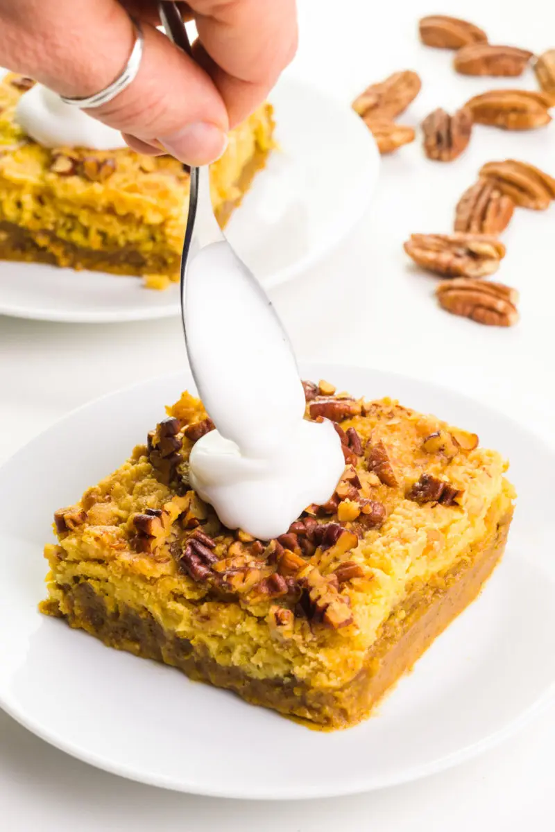 A hand holds a spoon adding a dollop over pumpkin crisp bars. There are nuts in the background.