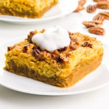 A pumpkin crisp bar has whipped cream on top. There is another bar in the background with pecans.