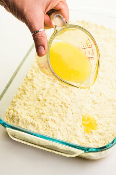 Melted butter is being poured over cake mix in a baking pan.