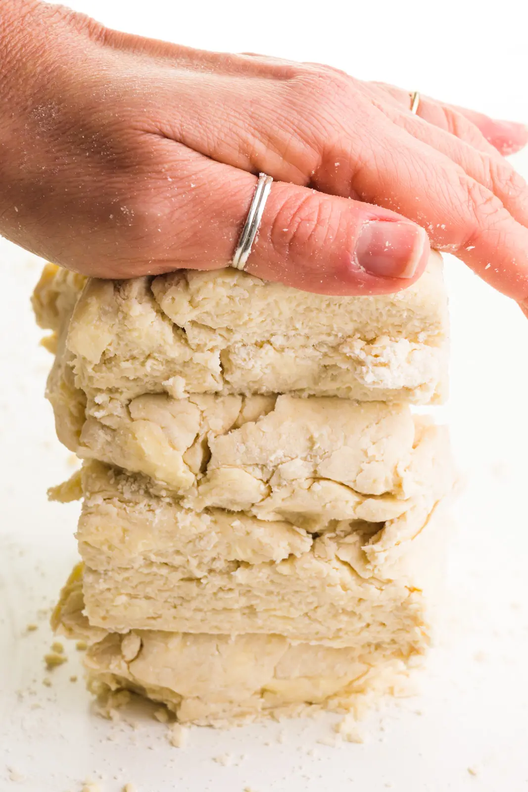 A hand pressed down on a stack biscuit dough.