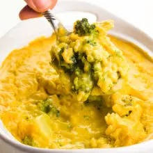 A hand holds a spoonful of vegan broccoli cheese casserole over the rest of the casserole dish.