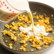 Vegan milk is being poured into a skillet with cooked onions and flour.