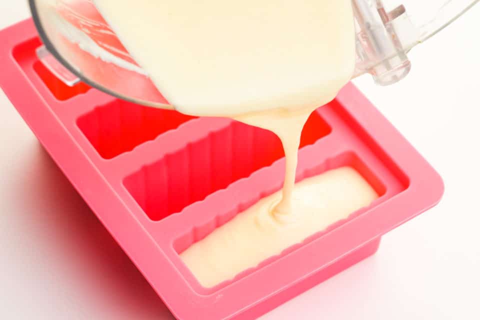 A vegan butter mixture is being poured into a pink silicone mold.