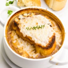 Looking down on a bowl of onion soup with a sprig of fresh thyme on the top and melted cheese.