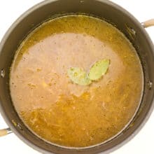 A pot is full of broth topped with two bay leaves.