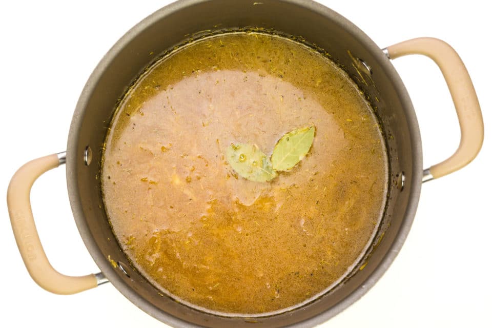 A pot is full of broth topped with two bay leaves.