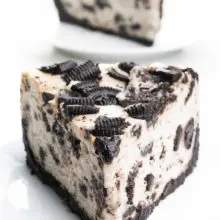 A slice of vegan Oreo cheesecake sits on a plate. Another slice is behind it.