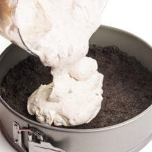 A creamy mixture is being poured into a springform pan with a chocolate cookie crust.