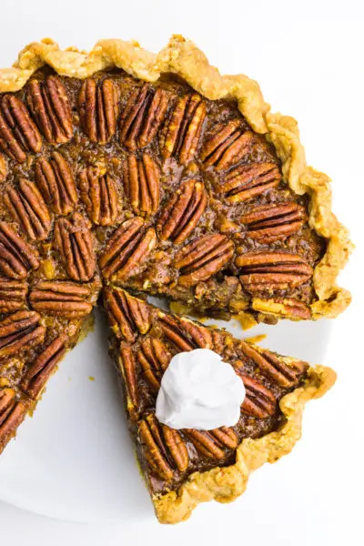 Looking down on a vegan pecan pie with a slice cut out. The slice has whipped cream on top.