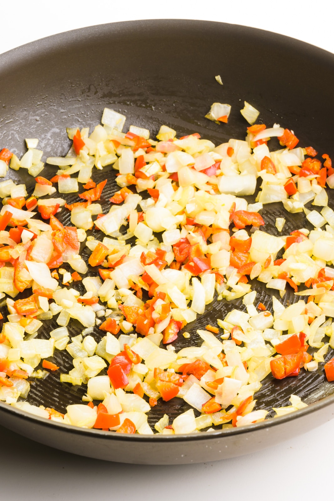 Diced onions and red peppers are in the bottom of a skillet being cooked.