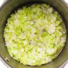 Onions and celery are cooking at the bottom of a saucepan.