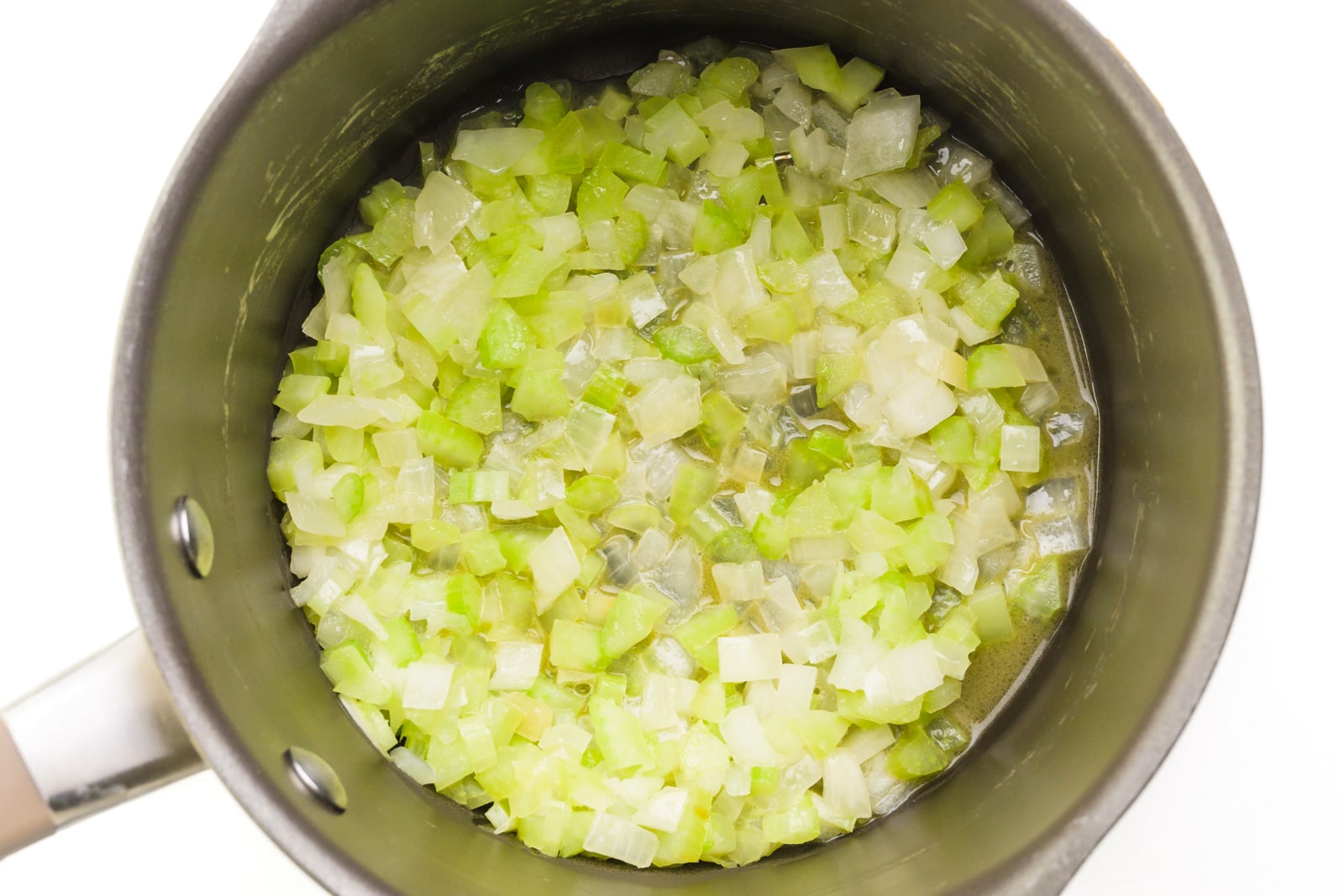 Onions and celery are cooking at the bottom of a saucepan.