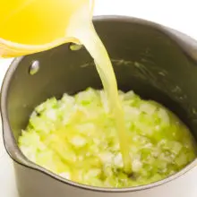 Vegetable broth is being poured into a skillet with cooked onions and celery in the bottom.