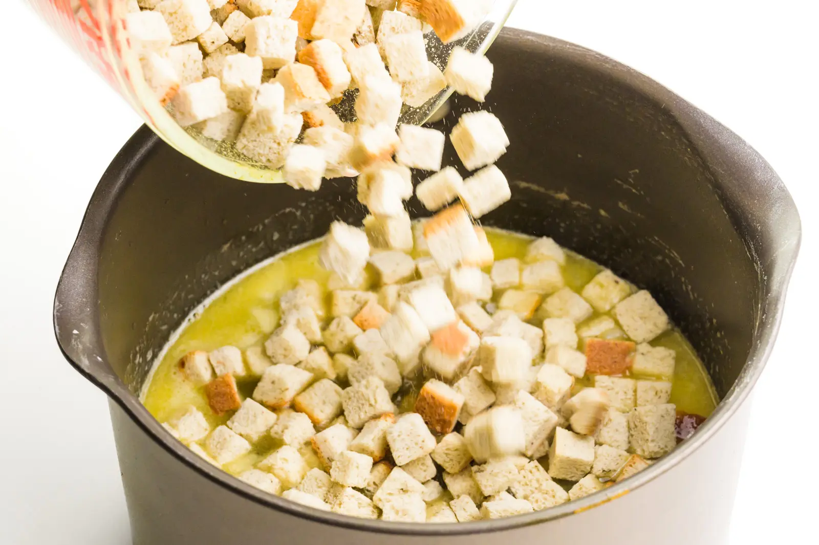 Stuffing mix is being poured into a pan with a vegetable broth mixture.