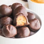 A bowl holds peanut butter balls, one with a bite taken out of it.