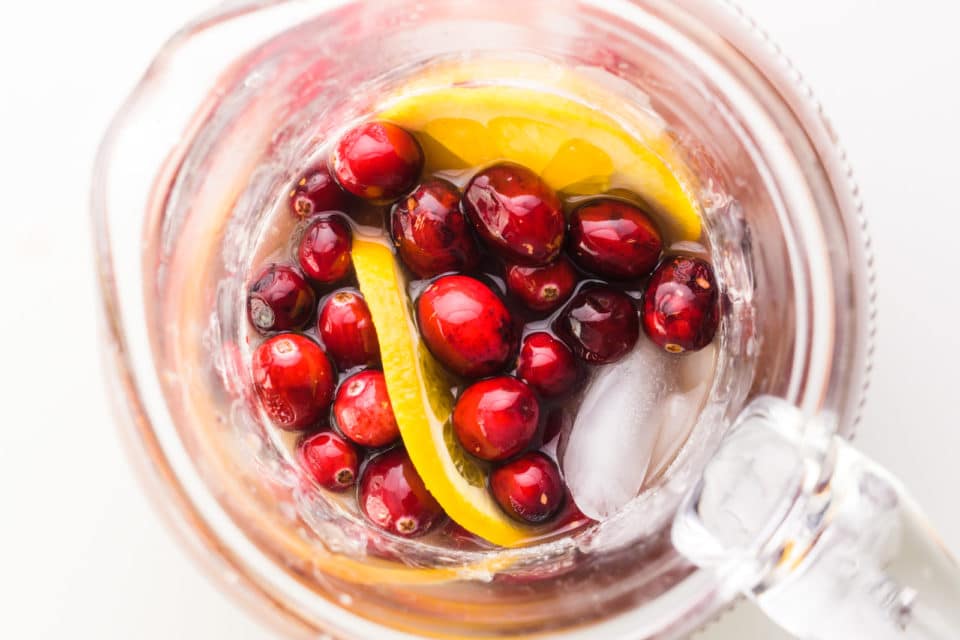 Looking down on a pitcher full of juices and topped with fresh cranberries and orange slices.