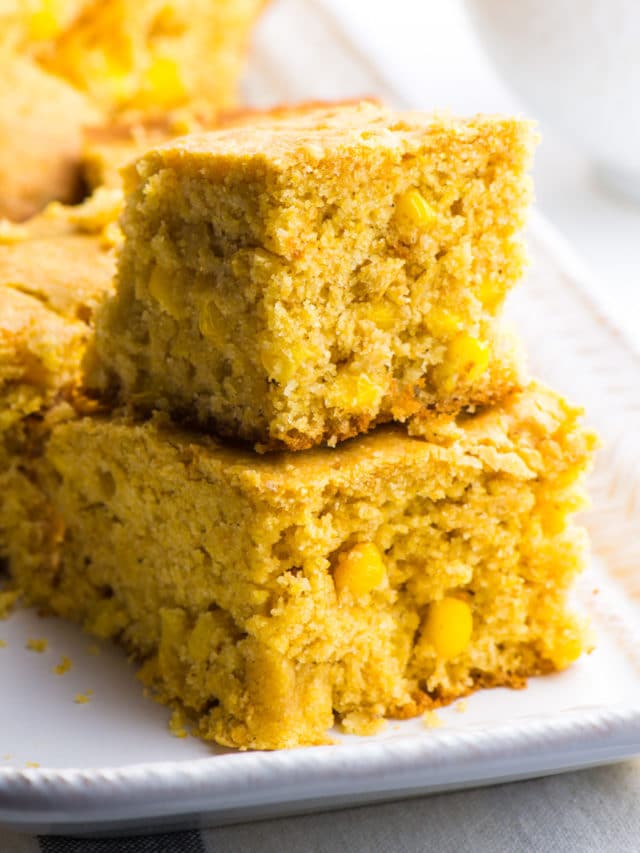 Two slices of vegan cornbread are stacked on top of each other with more slices in the background.