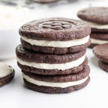 A stack of homemade Oreos sit nexts to a bowl of filling and more cookies around it.