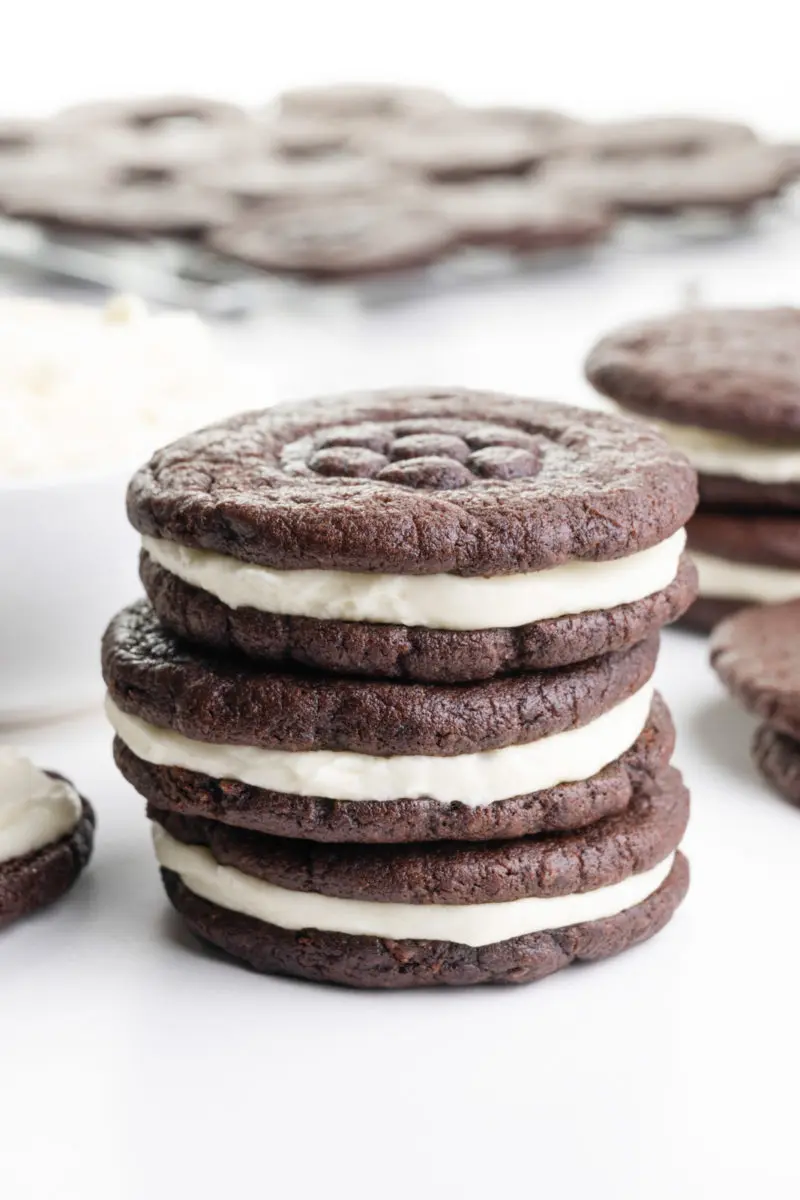 A stack of homemade Oreo cookies sits next to a bowl of filling and more cookies around and behind it.