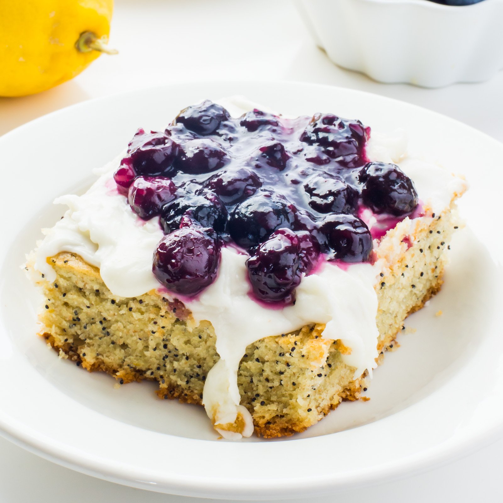A slice of lemon avocado cake with blueberry sauce on top sits on a plate