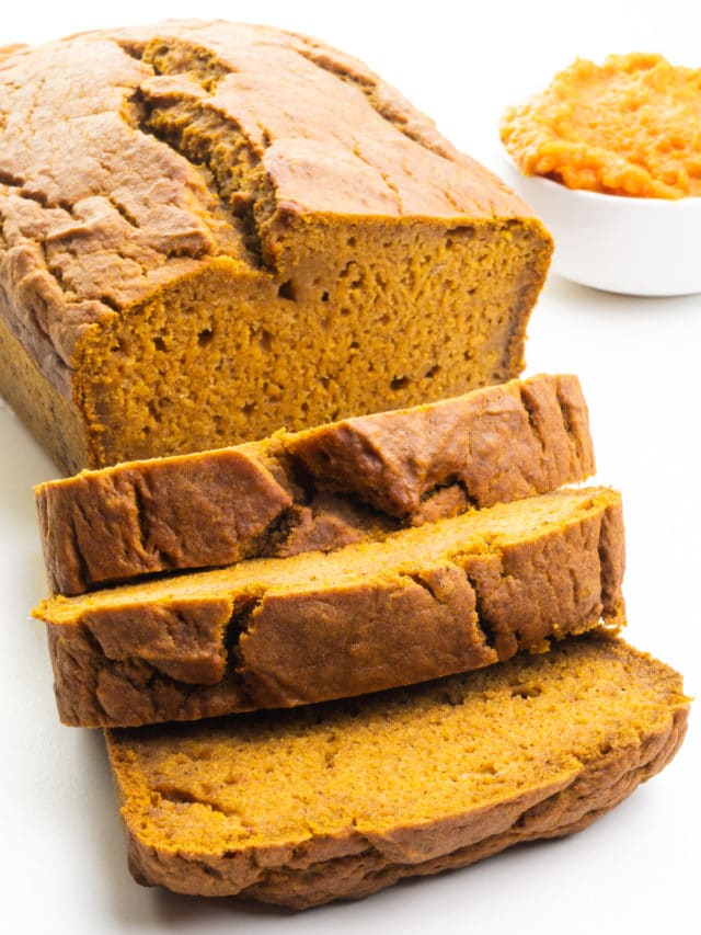 A loaf of vegan pumpkin bread has several slices cut. There's a bowl of Pumpkin Puree next to the loaf.