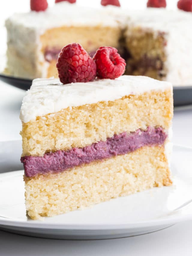 A slice of raspberry coconut cake on a plate sits in front of the rest of the cake.