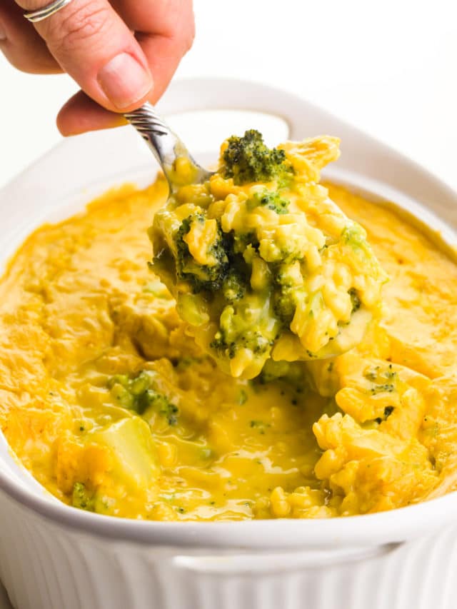 A hand holds a spoonful of vegan broccoli cheese casserole over the rest of the casserole dish.
